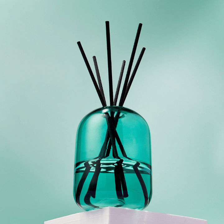 Green diffuser bottle with black reed sticks on a light green background