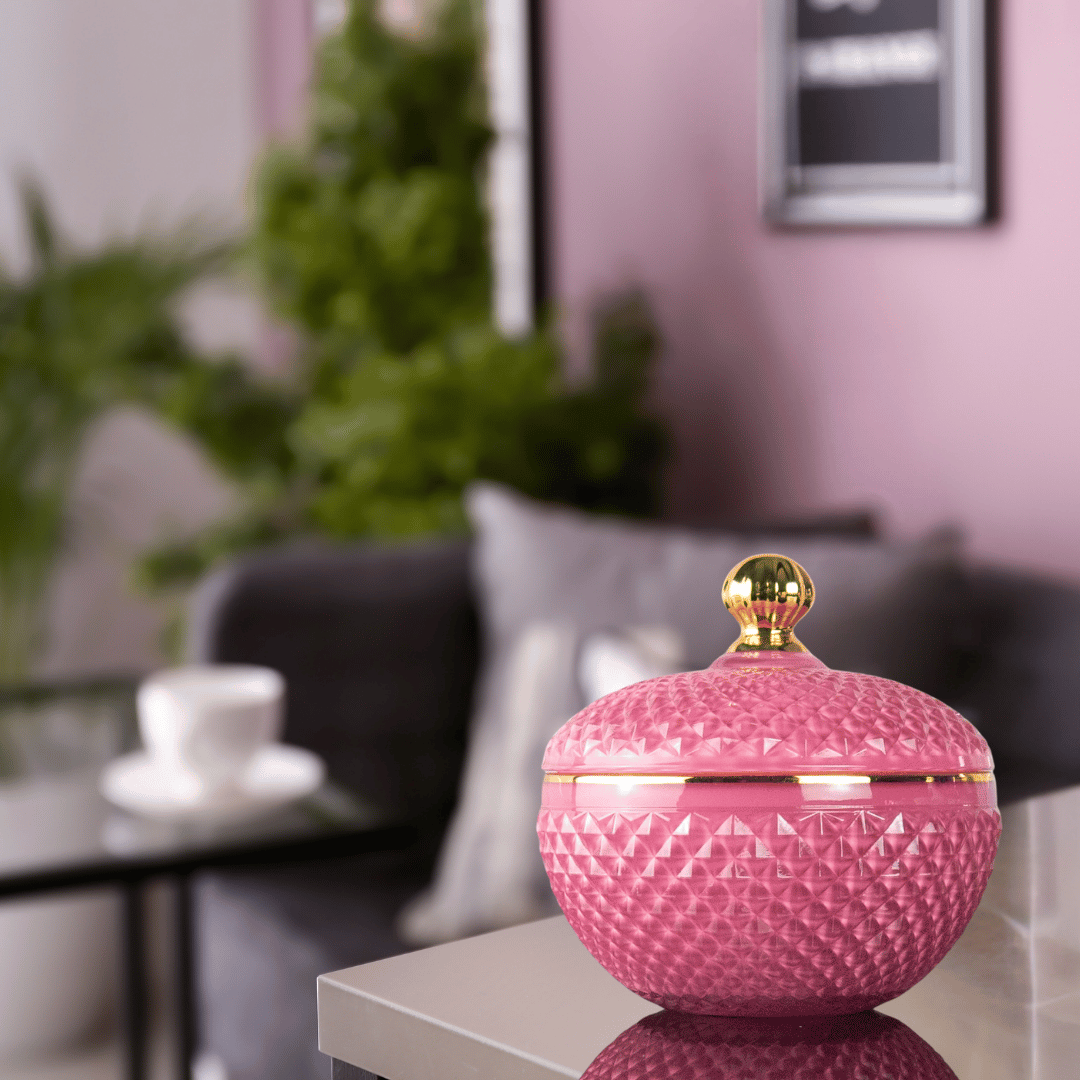 scented candle with 3 wicks in pink round, textured glass container, topped with a gold handled lid.